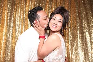 Happy client open air photo booth at wedding with gold sequin backdrop.